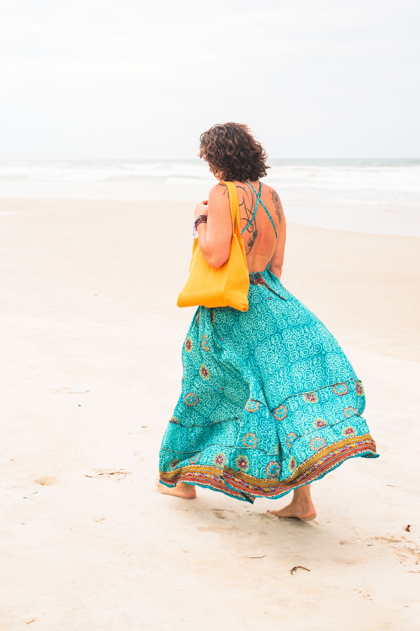 A woman walks barefoot on a wide ocean beach in Bahia.
