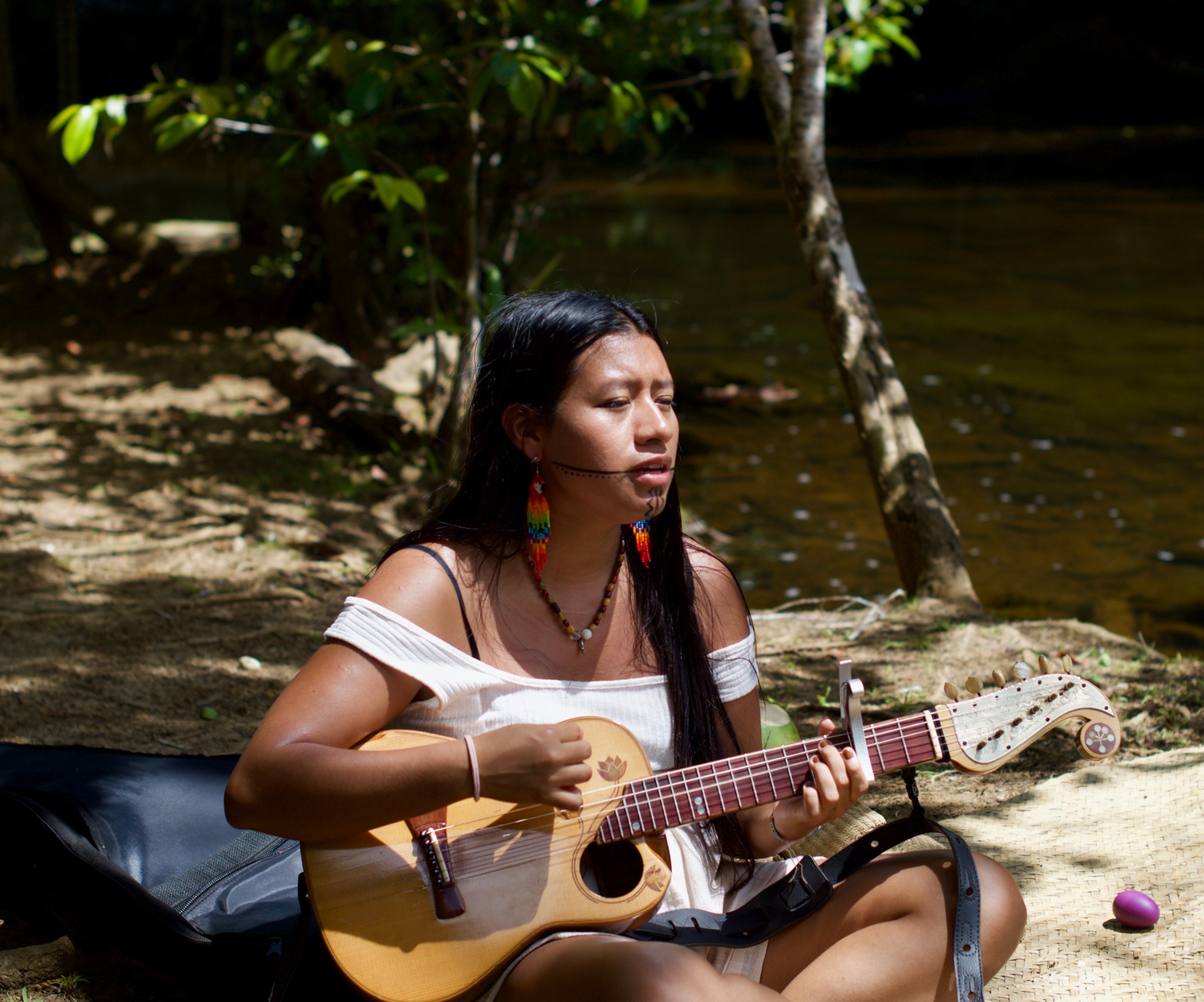 Guarani Mbya singer and composer Tainara Takua performs with her guitar outdoors.